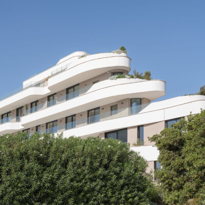 Fassade von the ONE Ibiza mit geschwungenen Balkonen hinter der Gartenbepflanzung.