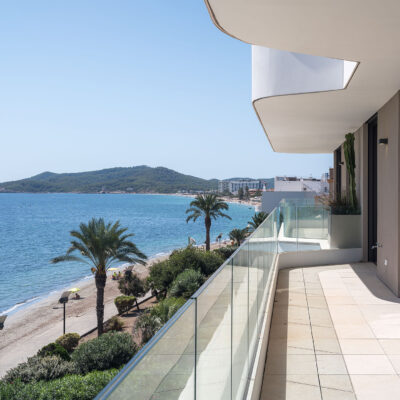 Terraza de the ONE Ibiza con barandilla de vidrio y vistas a la costa.